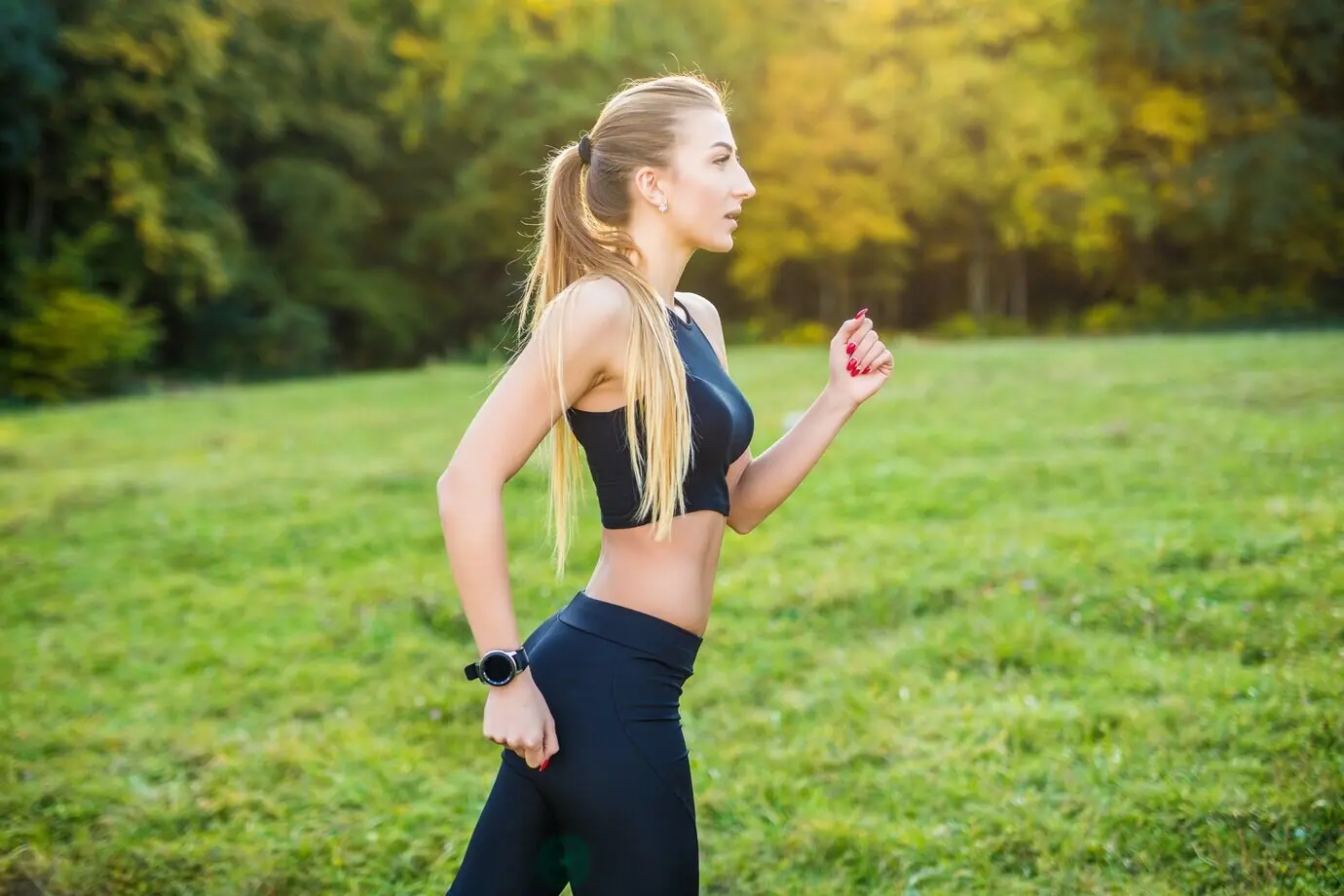 A Caucasian woman, a sports fitness model, jogging in a park in the sunshine on a beautiful summer day, training outdoors for a marathon.