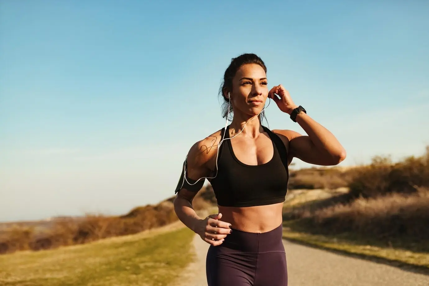 A young, athletic woman listens to music through earphones while jogging in nature, with copy space.