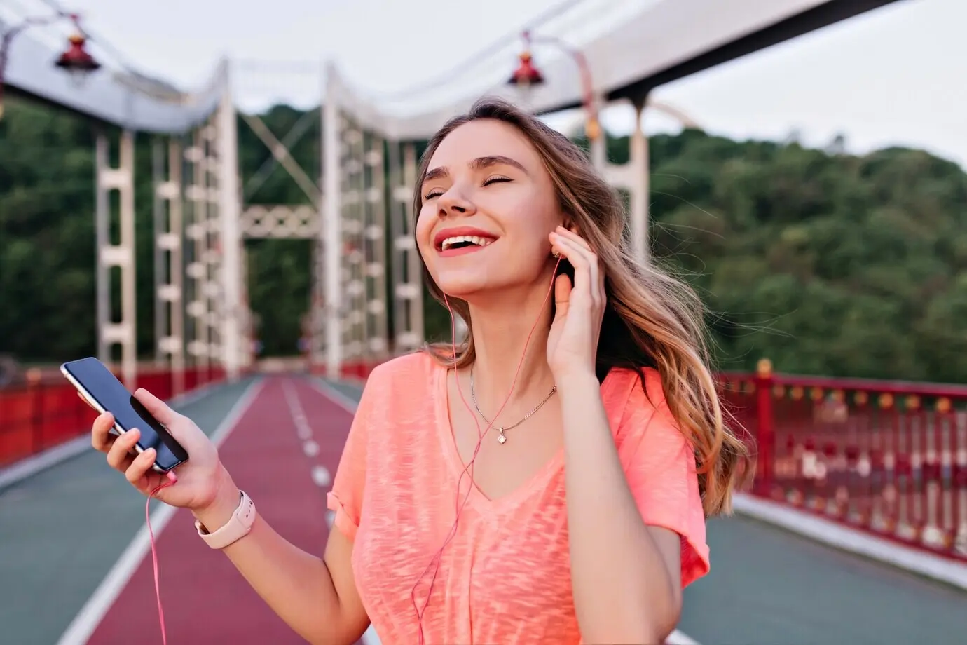 Elegant European woman listening to her favorite song with eyes closed while posing in a stadium. Charming girl in earphones relaxing after a marathon.