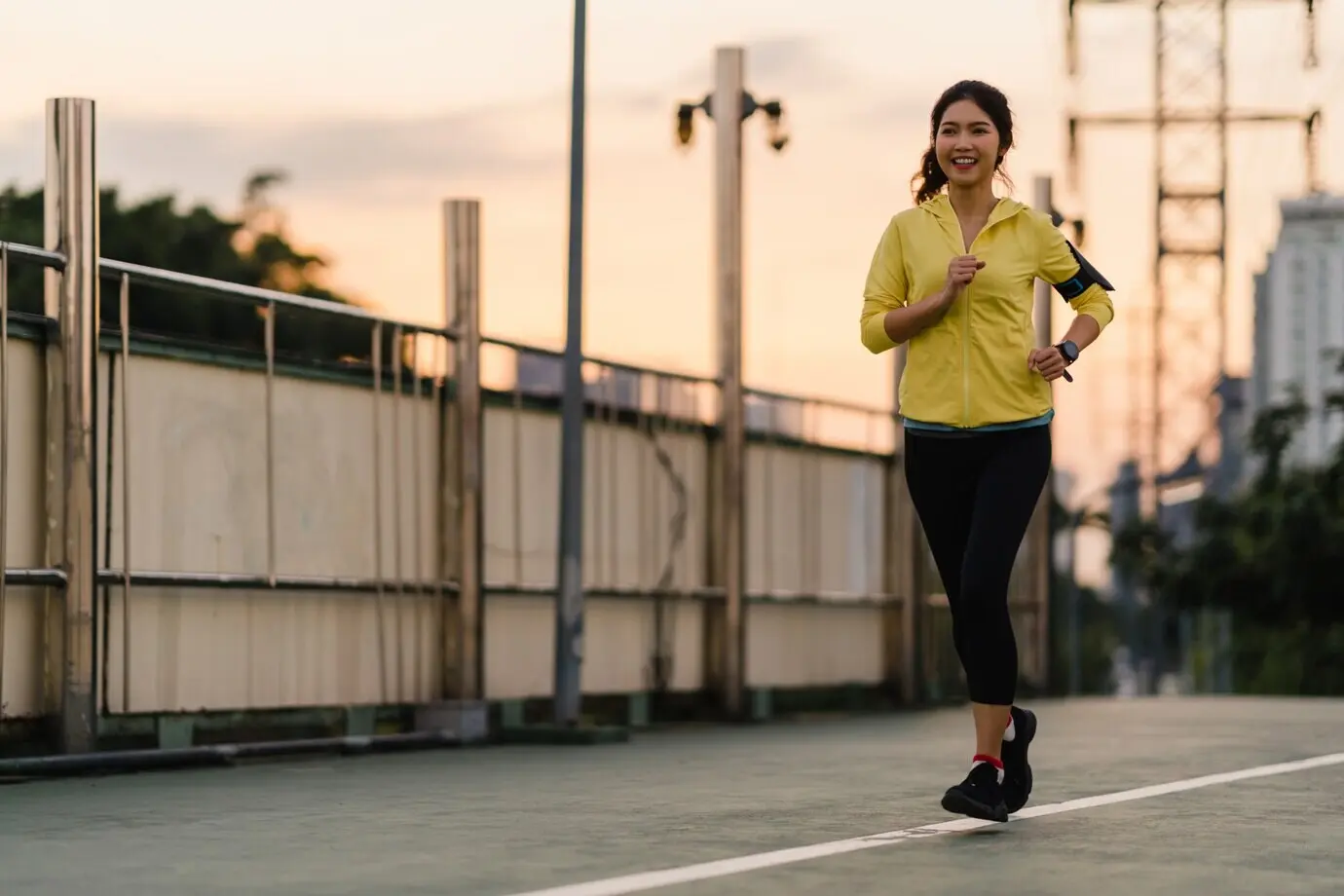 Beautiful young Asian female athlete doing running exercises in an urban setting. Japanese teenage girl wearing sportswear on a pedestrian bridge in the early morning. Active, sporty lifestyle in the city.